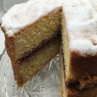 Victoria Sandwich Cake on a cake stand with a slice cut out